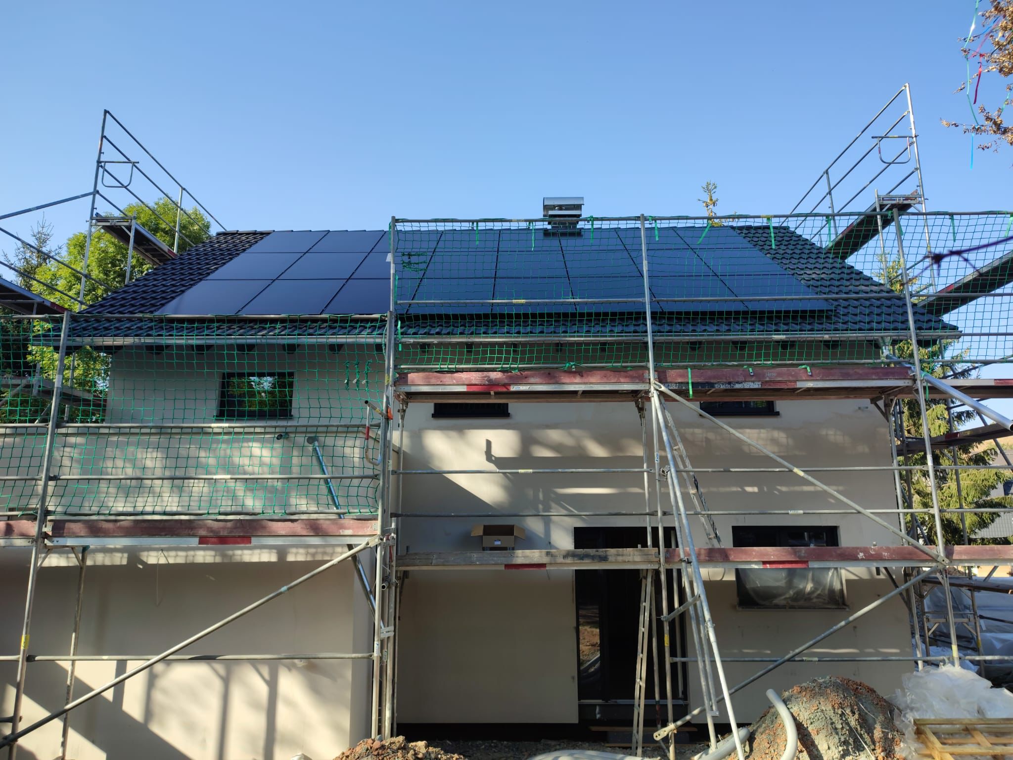 PV-Montage durch Dein Energiehaus Team: schwarze Module werden auf dem eingerüsteten Dach eines Neubaus in Neuss installiert